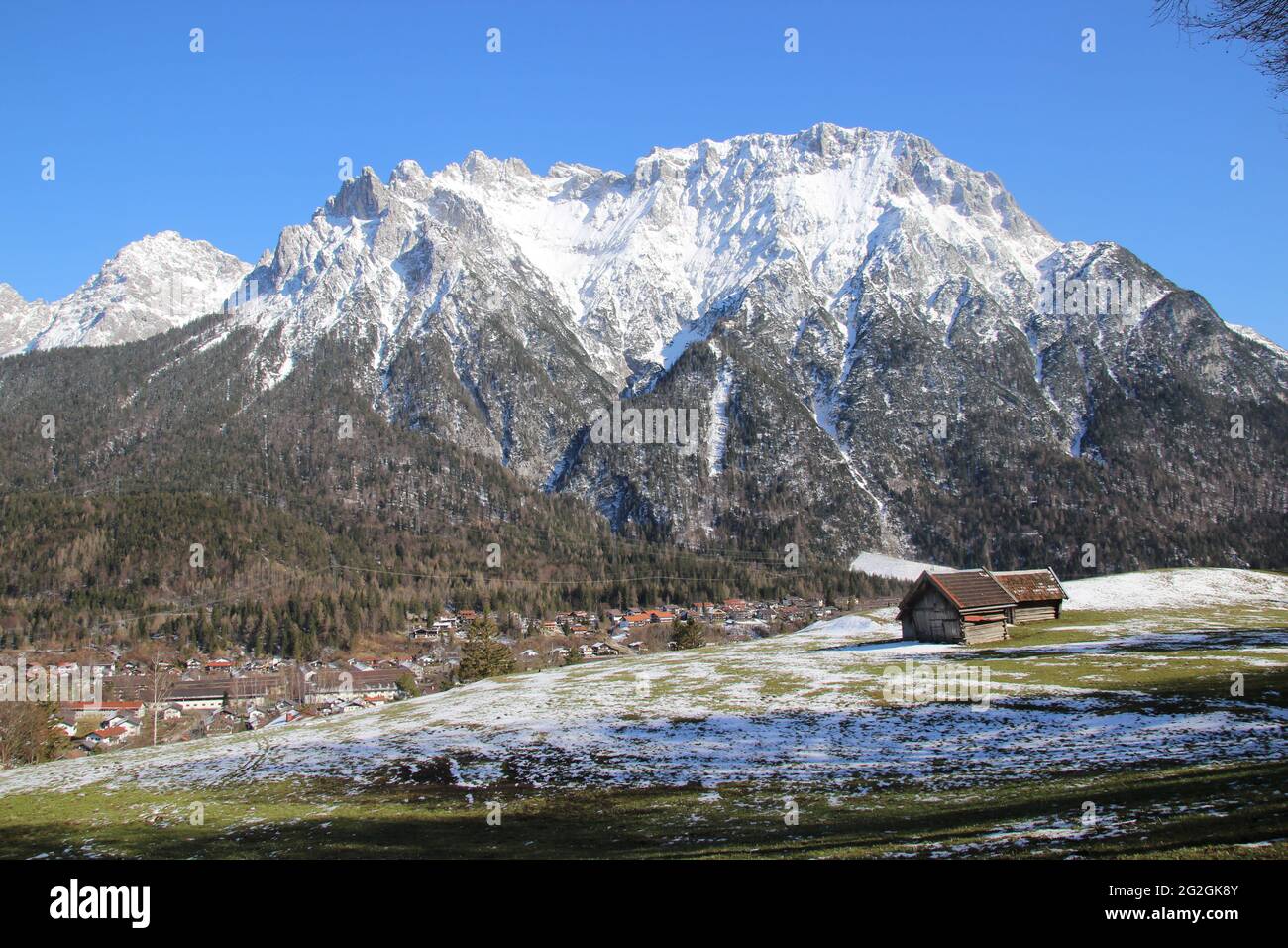 Passeggiata primaverile nei pressi di Mittenwald, i Monti Karwendel tutti in bianco, in primo piano il prato primaverile leggermente innevato con fienile, panoramica della zona, Europa, Germania, Baviera, alta Baviera, Werdenfels, inverno, Monti Karwendel, chiesa Foto Stock