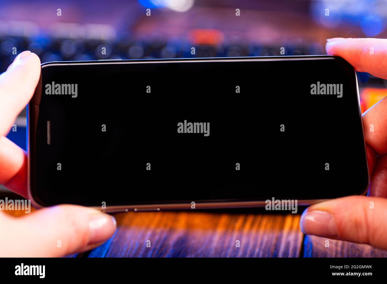 Tenere le mani sullo smartphone moderno con schermo nero sullo sfondo del computer portatile. Foto Stock