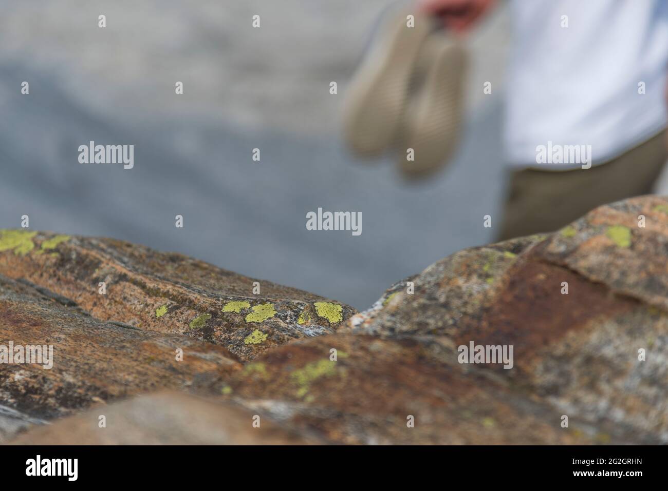 Impressioni da Lavertezzo in Val Verzasca, Locarno, Canton Ticino in Svizzera: Meta turistica molto apprezzata per escursioni, immersioni e nuoto. Lichene sul granito, sullo sfondo una persona a piedi nudi con scarpe in mano. Foto Stock