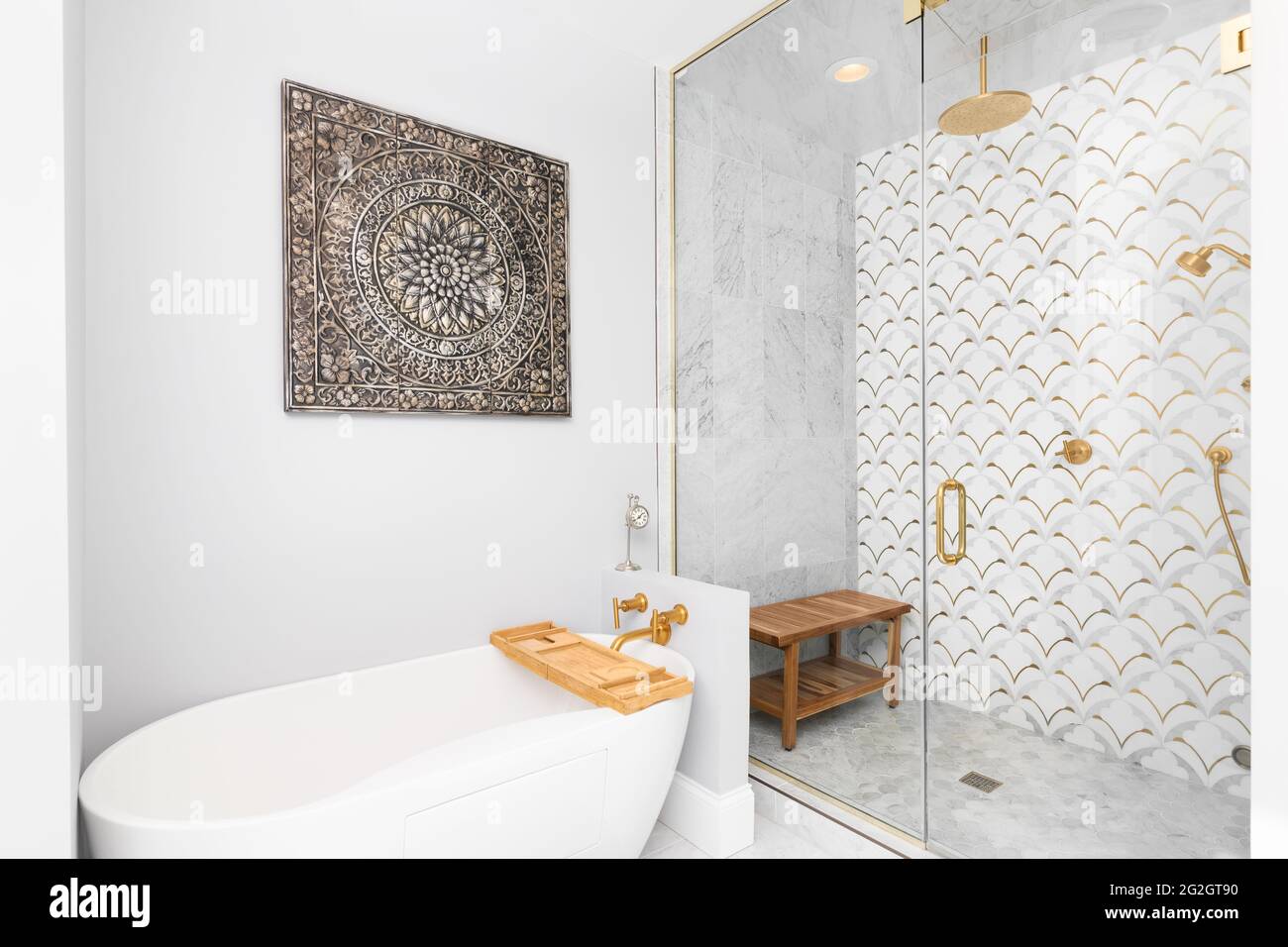 Una bella doccia e vasca piastrellata con piastrelle bianche e dorate sulle pareti, piastrelle di marmo mosaico sul pavimento, e soffione doccia e bulloneria dorati. Foto Stock