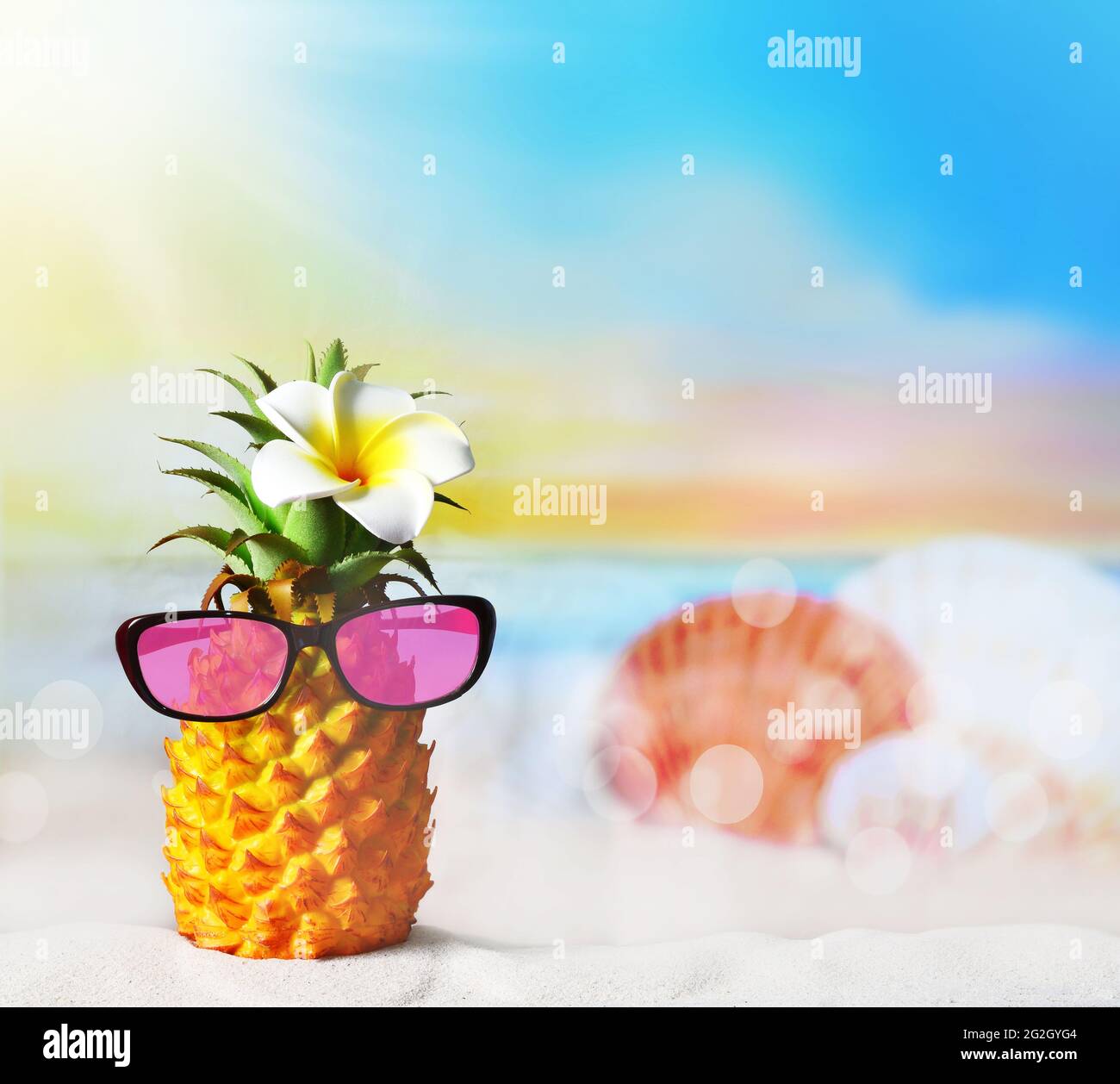 Ananas con fiori e occhiali da sole in spiaggia. Concetto di spiaggia estiva. Foto Stock