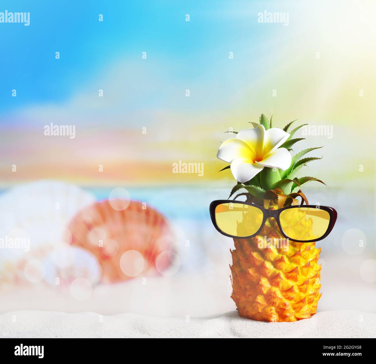 Ananas con fiori e occhiali da sole in spiaggia. Concetto di spiaggia estiva. Foto Stock