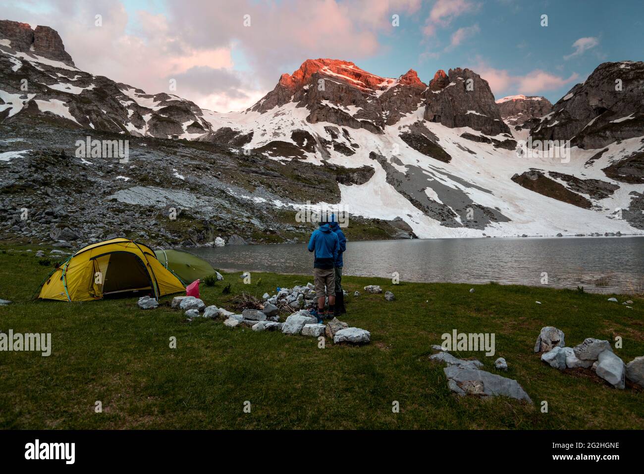 Due escursionisti si trovano di fronte a un lago di montagna, mentre il sole illumina le cime più alte delle montagne del Parco Nazionale Prokletije Foto Stock