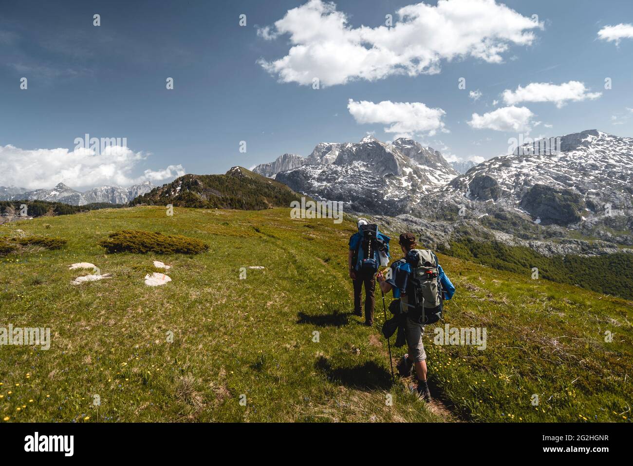 Due escursionisti su uno stretto sentiero battuto camminano verso le montagne del Parco Nazionale di Prokletije sotto il sole Foto Stock