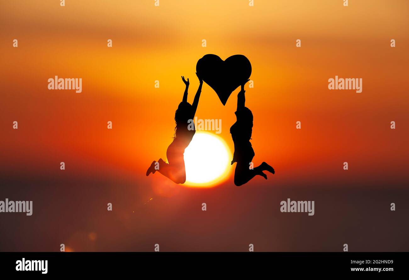 Due donne saltano con un cuore davanti al disco del sole Foto Stock