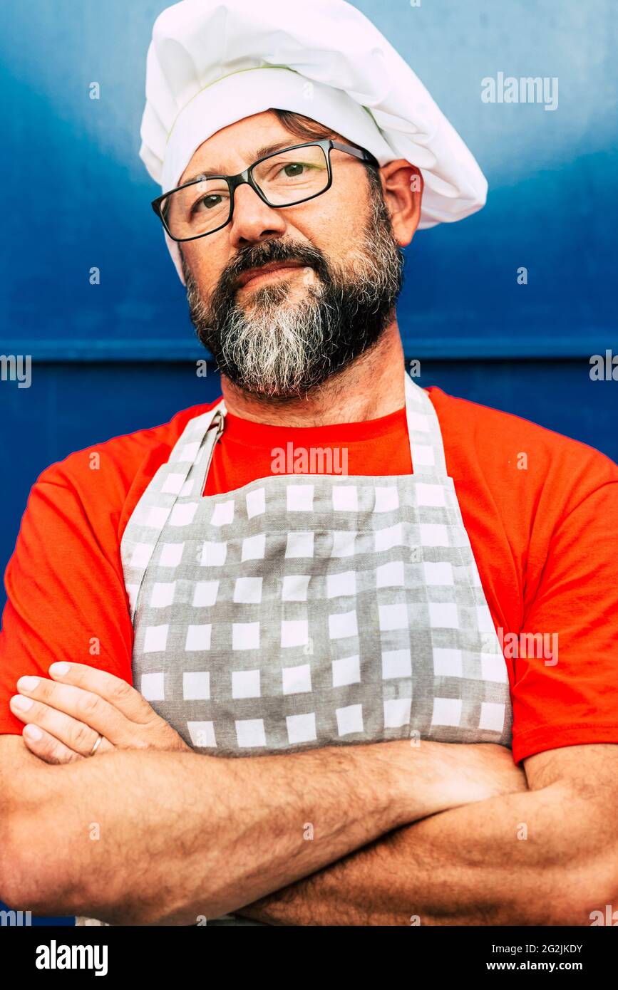 Ritratto di un uomo portatore di hipster chef adulto che guarda sulla macchina fotografica e indossa cappello bianco - concetto di ristorante o caffè e le persone che lavorano su di esso - vetri e rosso blu immagine colori Foto Stock