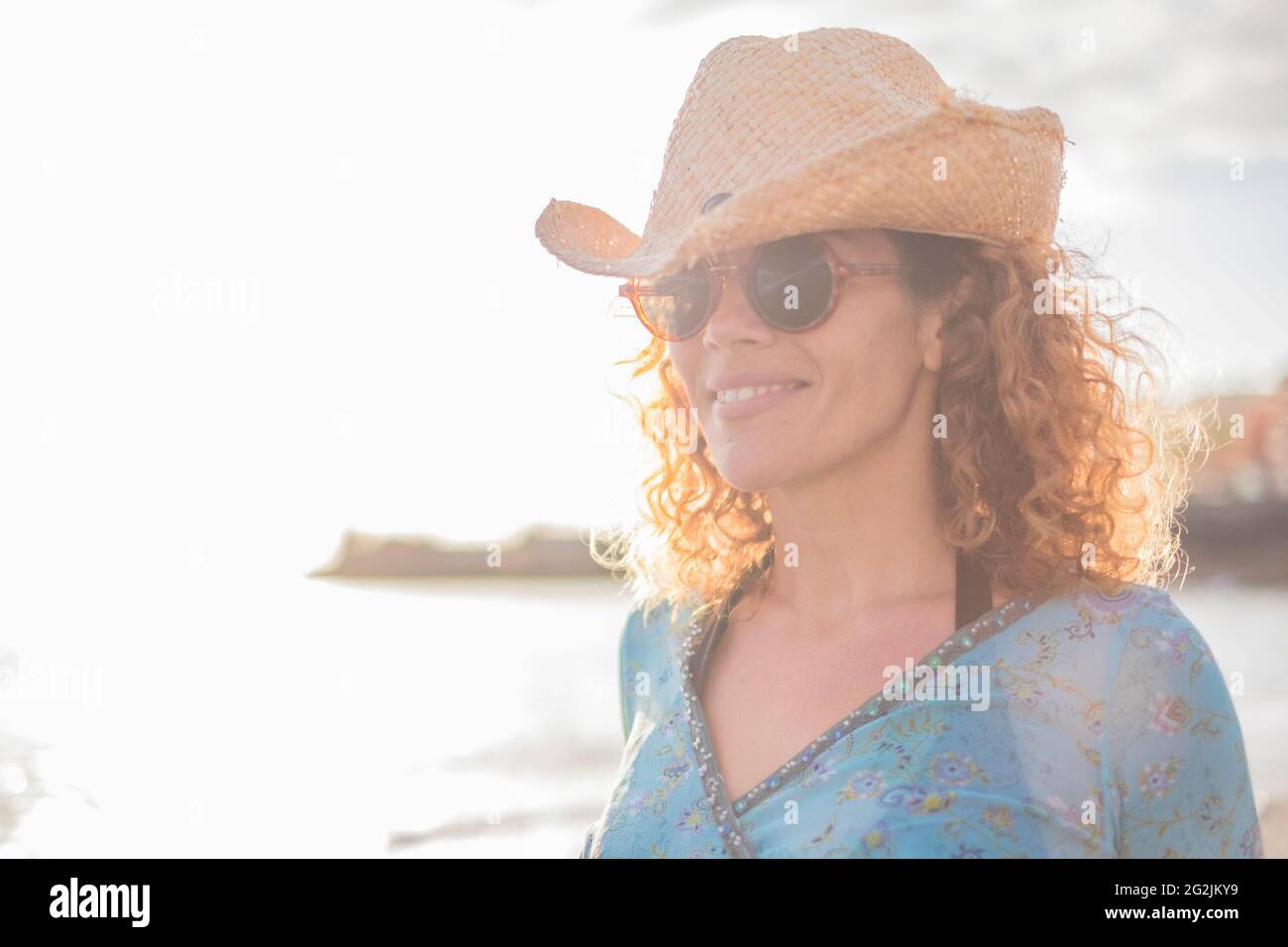 Ritratto di allegra donna adulta di mezza età allegra sorridente e godente all'aperto - giovane donna caucasica con cappello e occhiali da sole - spiaggia oceanica in sfondo sfocato Foto Stock