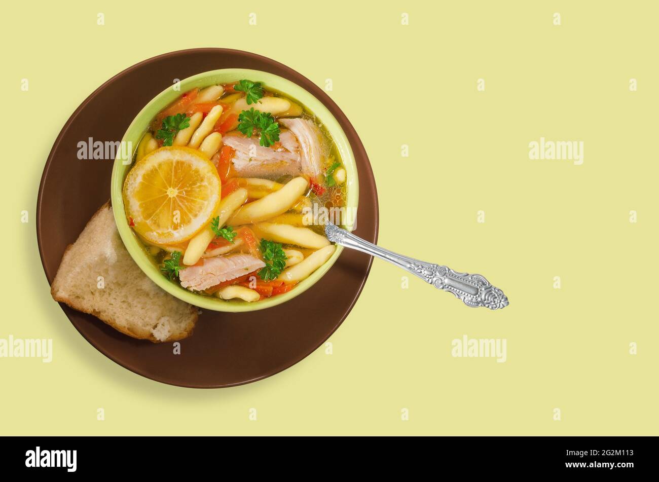 Una ciotola di zuppa di pollo con erbe e limone, su uno sfondo verde chiaro Foto Stock