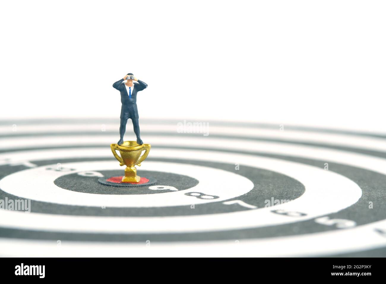 Uomini d'affari in piedi sopra trofeo d'oro su dartboard utilizzando binocoli. Fotographia dei giocattoli delle piccole persone in miniatura. Isolato su sfondo bianco. Foto Stock