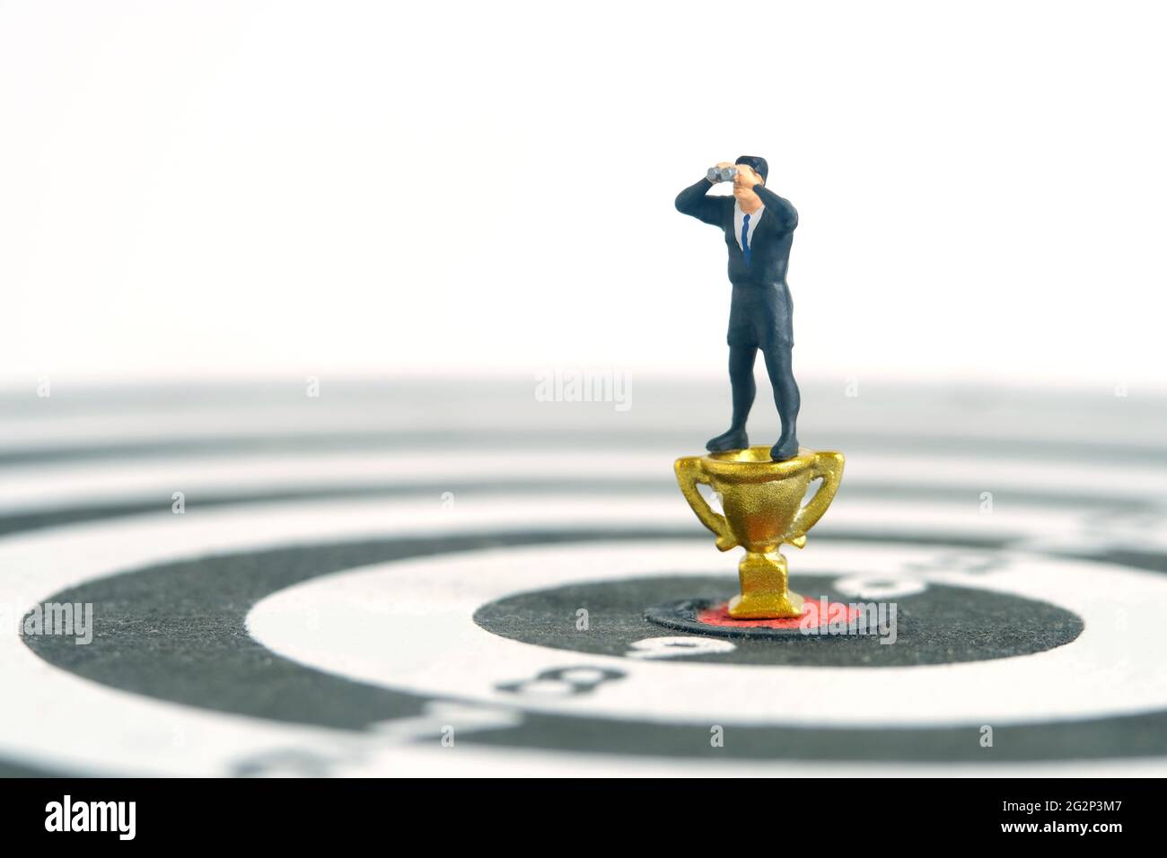 Uomini d'affari in piedi sopra trofeo d'oro su dartboard utilizzando binocoli. Fotographia dei giocattoli delle piccole persone in miniatura. Isolato su sfondo bianco. Foto Stock