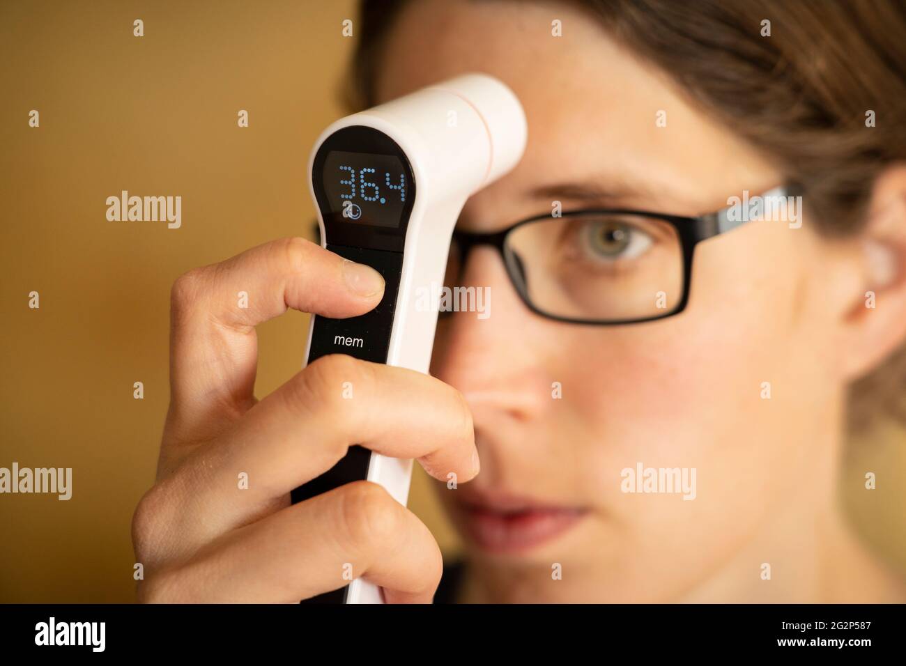Una giovane donna tra i suoi trent'anni che ha la diagnosi di febbre prendendo la propria temperatura con un termometro digitale a infrarossi. REGNO UNITO Foto Stock
