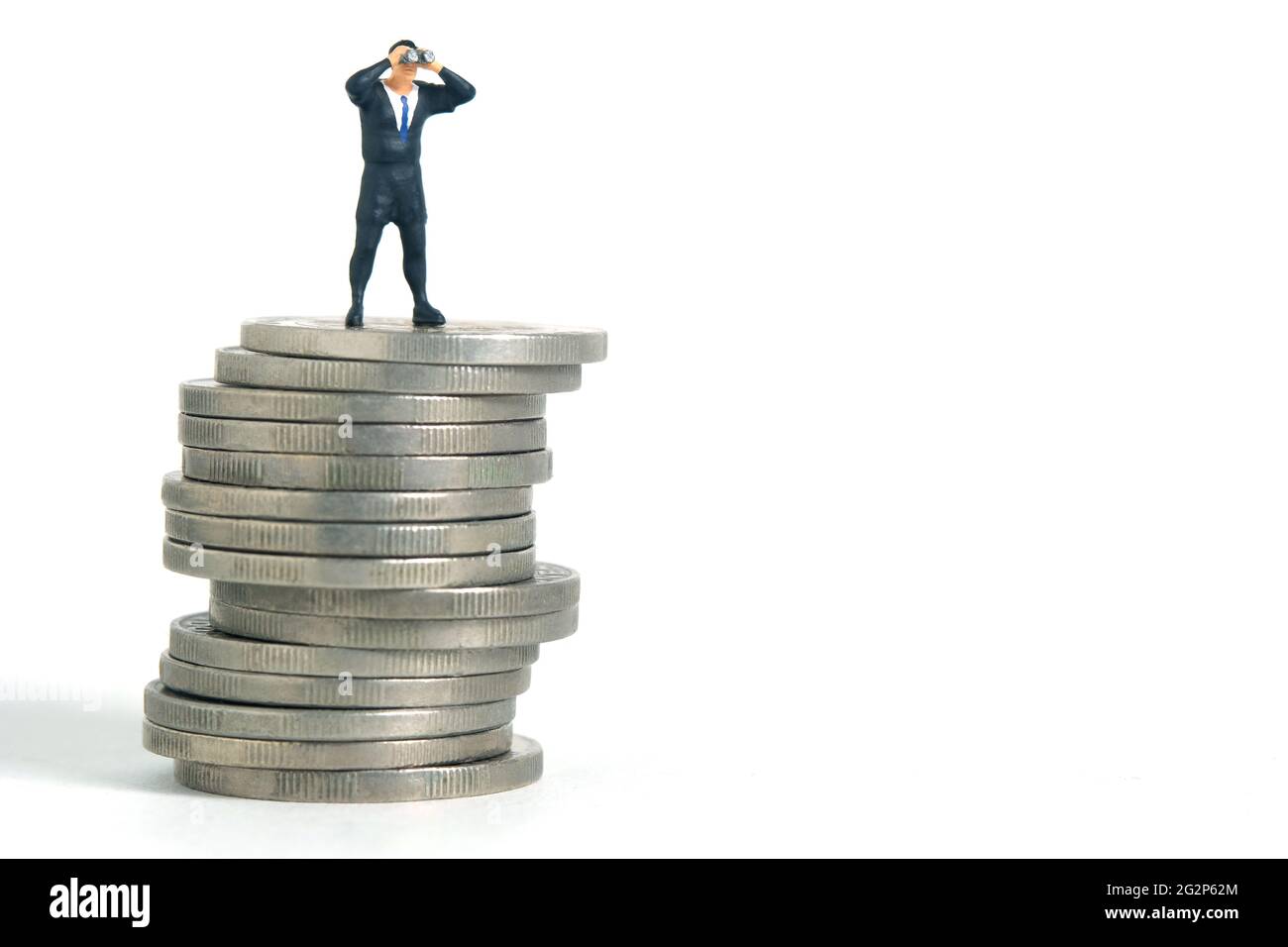 Uomini d'affari che usano binocoli in piedi sopra il mucchio di monete. Fotographia dei giocattoli delle piccole persone in miniatura. Isolato su sfondo bianco Foto Stock