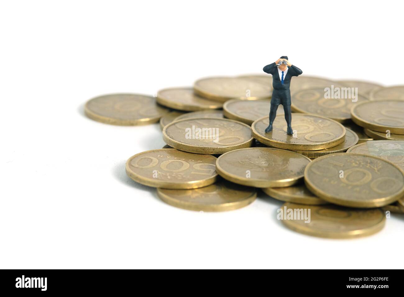 Uomo d'affari che usa il binocolo in piedi sopra il mucchio di moneta. Fotographia dei giocattoli delle piccole persone in miniatura. Isolato su sfondo bianco Foto Stock