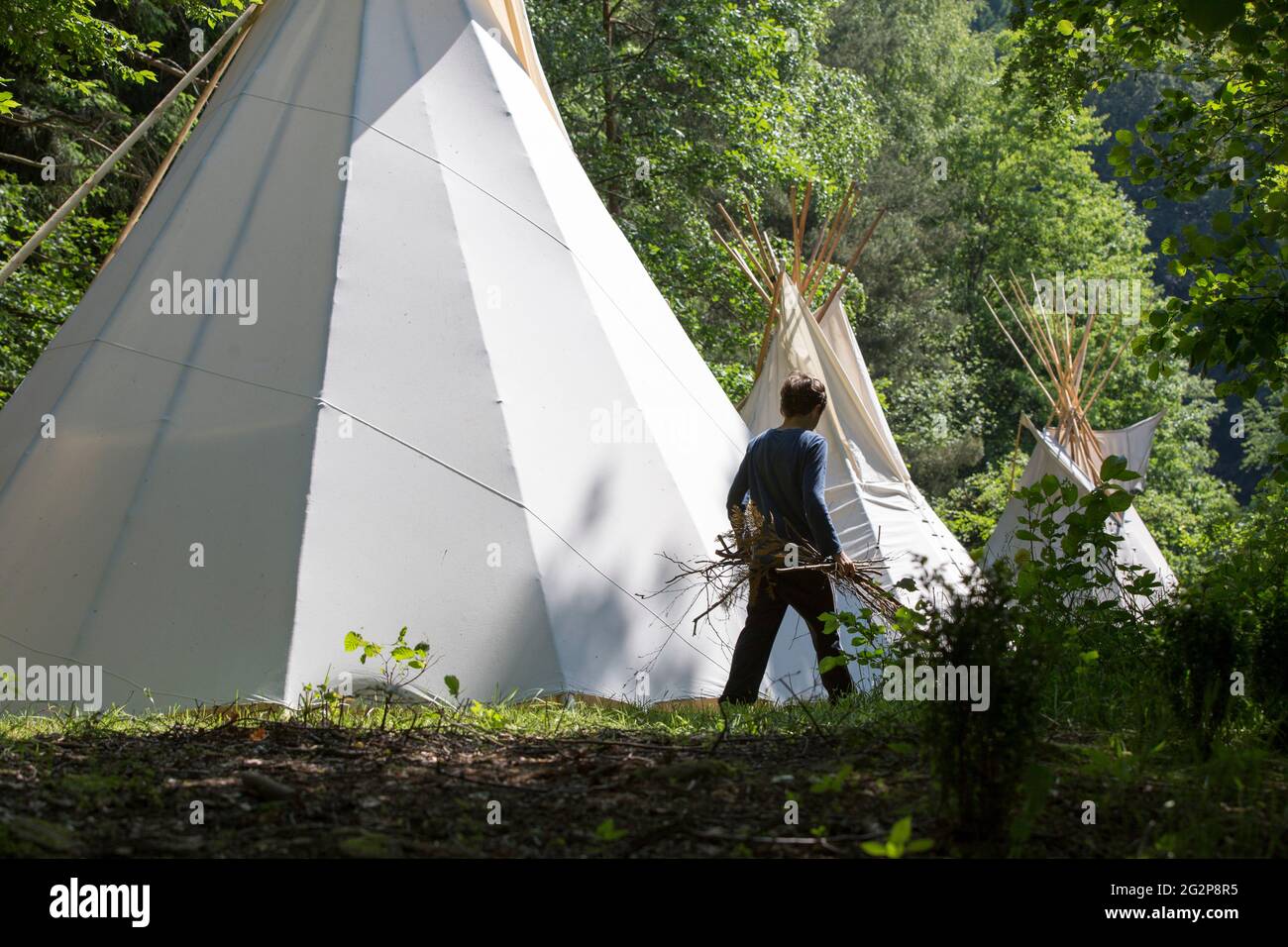 Un adolescente con legna da ardere in mano di fronte a tipis in un campo estivo a Gemany Foto Stock