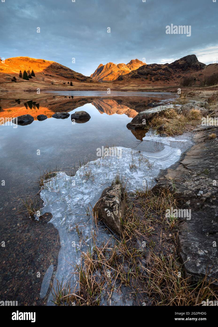 Splendida mattina invernale a Blea Tarn nel Lake District inglese con luce dorata sulle montagne e riflessi perfetti sull'acqua. Foto Stock