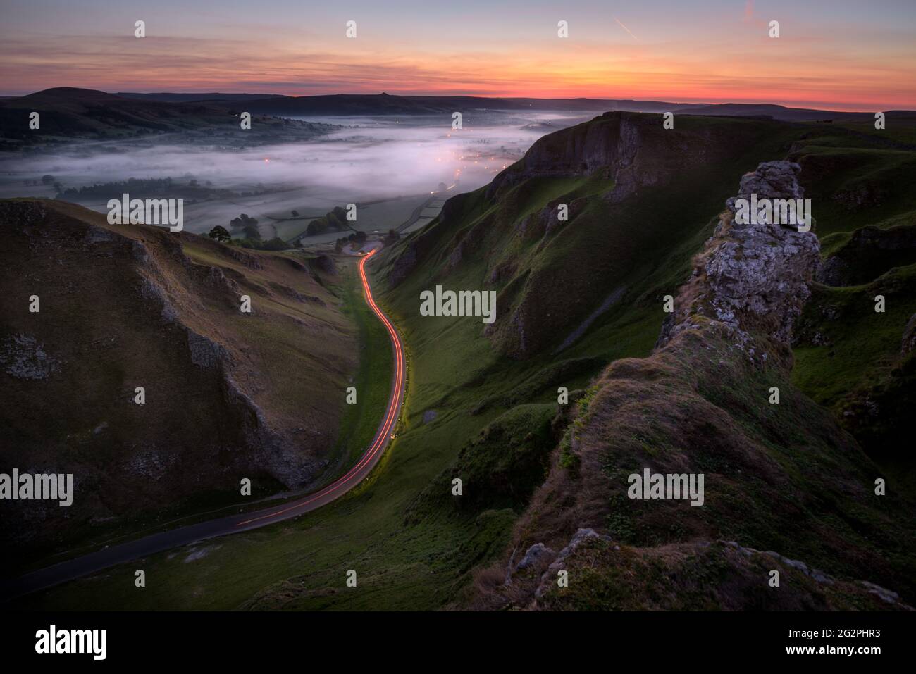 Sentieri leggeri per auto al passo Winnats con nebbia nella valle prima dell'alba. Peak District, Regno Unito. Foto Stock