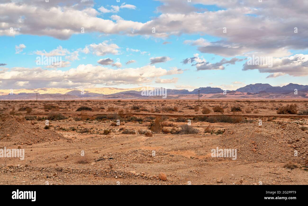 Paesaggio tipico al confine con Israele e Giordania. Deserto asciutto pianeggiante con cespugli bassi e piccole montagne, il sole splende attraverso le nuvole serali Foto Stock