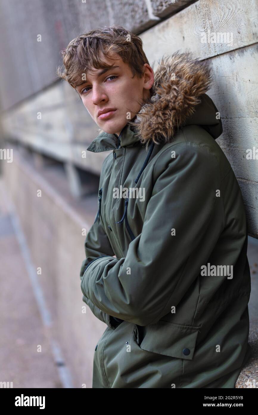 Giovane adolescente maschile adulto che indossa una giacca parka all'esterno in un ambiente urbano moderno Foto Stock