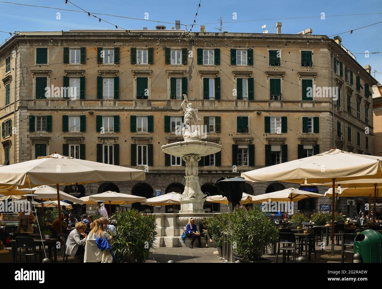 Piazza Colombo con l'antica fontana (1646) al centro e caffè all'aperto sotto i raggi del sole, Genova, Liguria, Italia Foto Stock