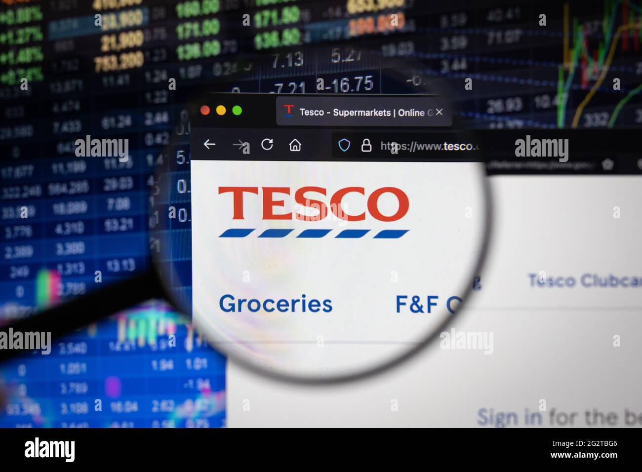 Logo aziendale Tesco su un sito Web con sviluppi sfocati del mercato azionario sullo sfondo, visto su uno schermo del computer attraverso una lente di ingrandimento Foto Stock
