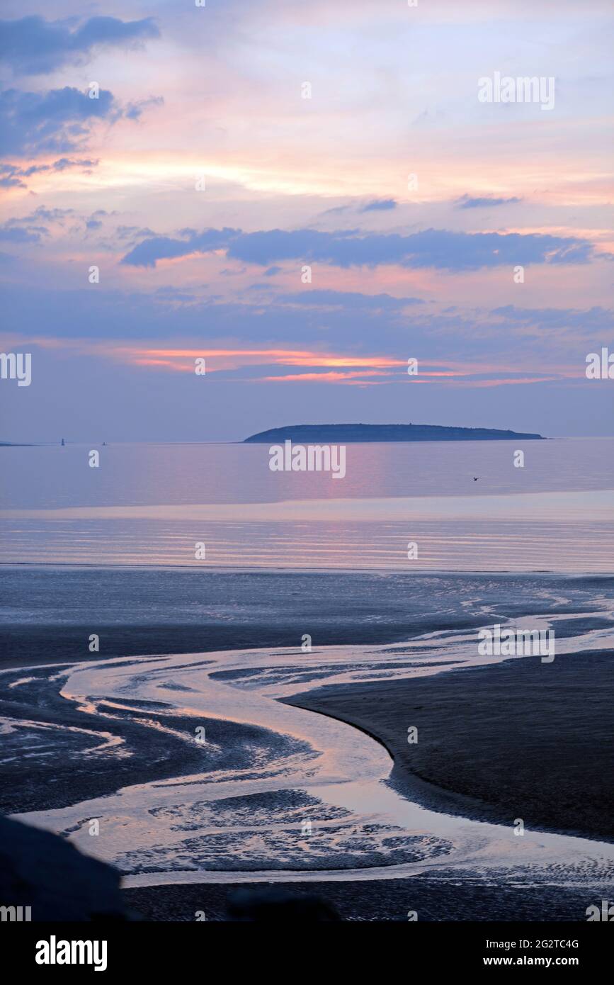 Puffin Island e i colori del sole che tramonta da Penmaenmawr Beach, Anglesey, Galles del Nord. Foto Stock