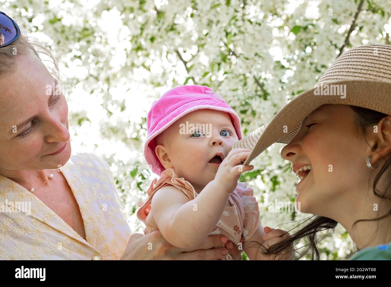 Felice fotografia di stile di vita familiare. Mamma sorridente e le sue due figlie felici e carine su un giardino di primavera fiorente. Concetto di infanzia e maternità. Verde Foto Stock