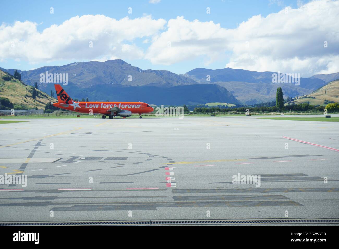 Queenstown, Nuova Zelanda - 6 marzo 2015; le montagne formano lo sfondo di un aereo di colore arancione che arriva all'aeroporto. Foto Stock