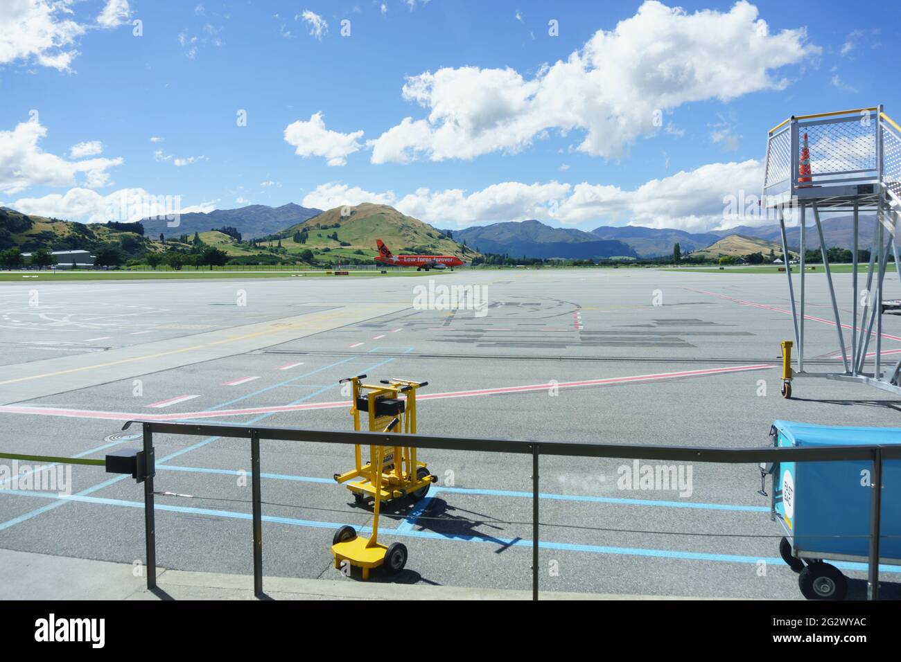 Queenstown, Nuova Zelanda - 6 marzo 2015; le montagne formano lo sfondo di un aereo di colore arancione che arriva all'aeroporto in lontananza attraverso il asfalto. Foto Stock