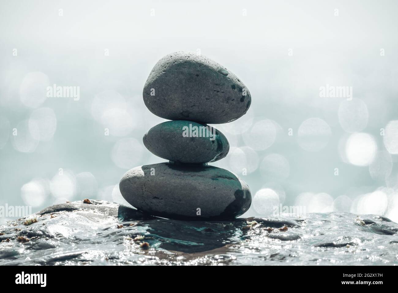 Equilibrata piramide di ciottoli sulla spiaggia in una giornata di sole. Abstract Sea bokeh sullo sfondo. Messa a fuoco selettiva. Pietre Zen sulla spiaggia di mare, meditazione Foto Stock