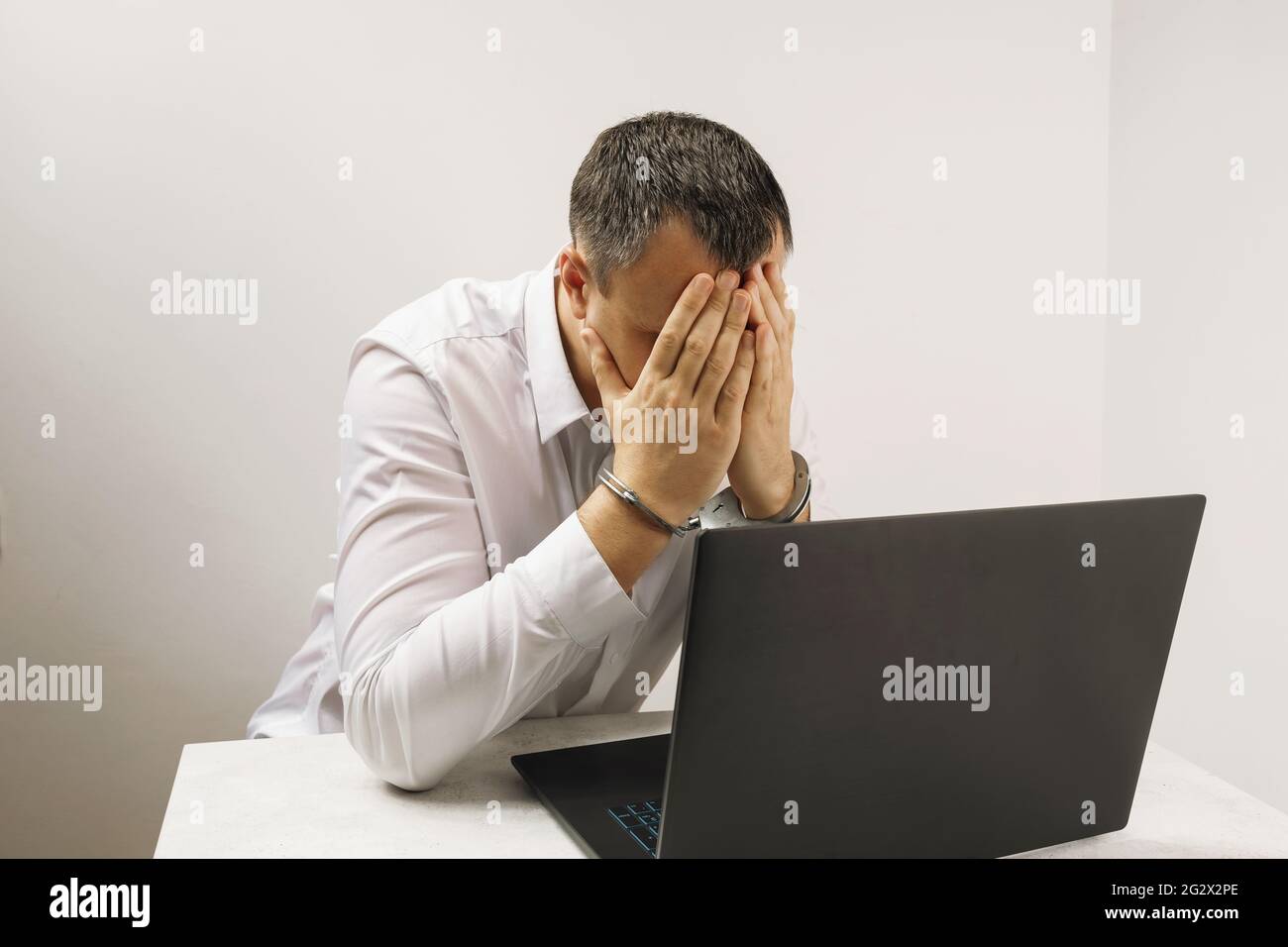 Un hacker in manette vicino a un computer portatile, copre il suo volto con le mani, un concetto sul tema dei crimini informatici. Foto Stock