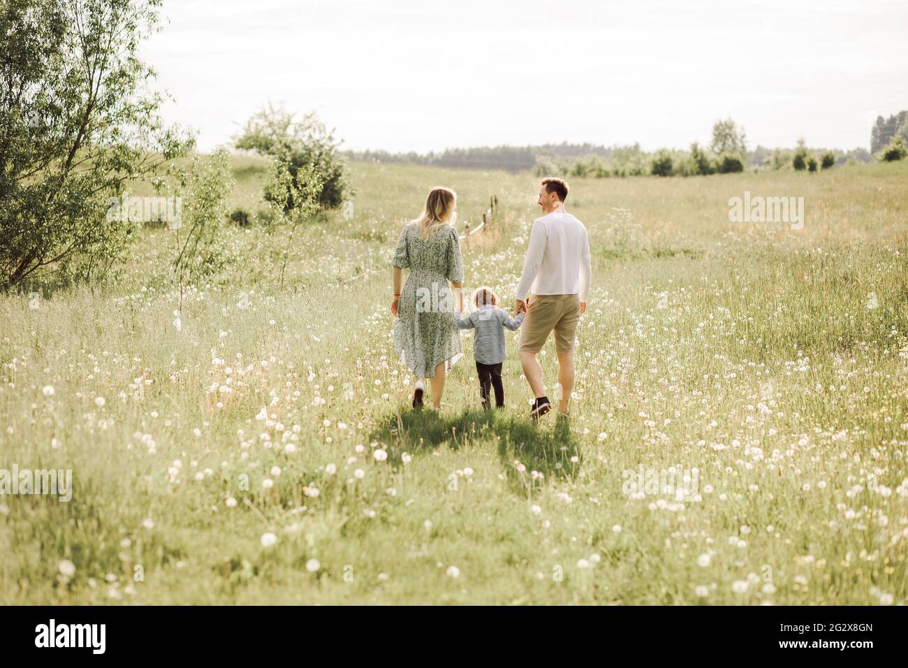 famiglia felice a piedi in prato di fiori fioriti da dietro, mamma papà e figlio, vista posteriore foto Foto Stock