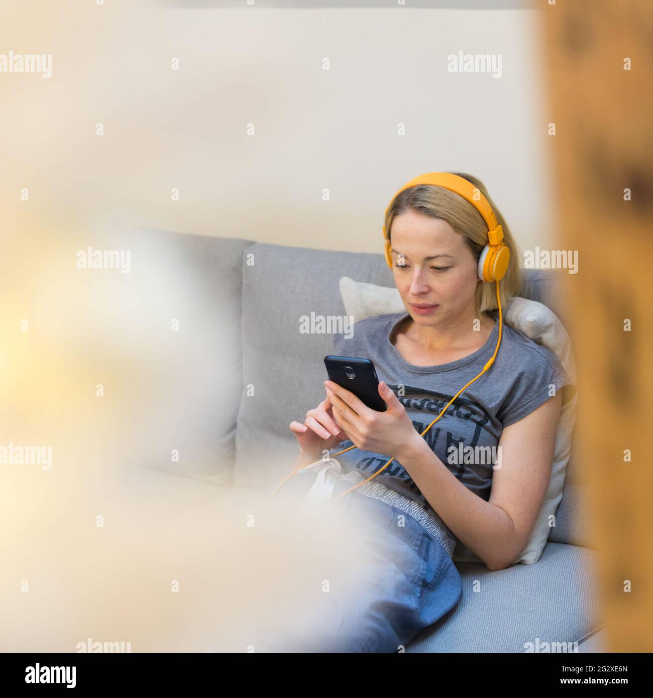 Giovane donna pensierosa seduta all'interno sul divano del soggiorno di casa utilizzo dei social media sul telefono per le chat video e la permanenza collegato con la sua amata Foto Stock