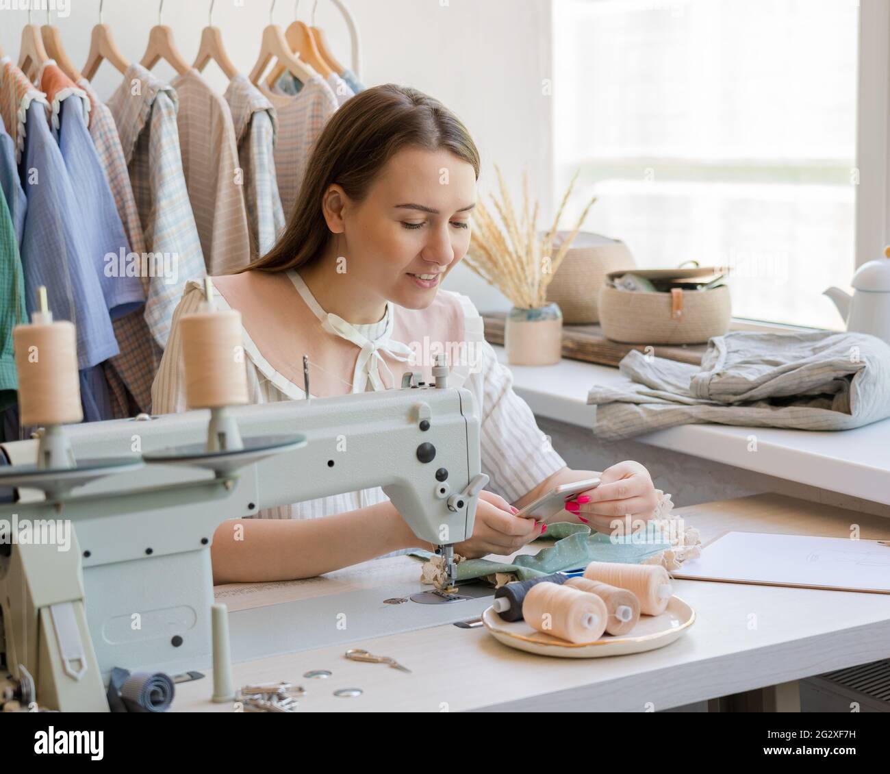 Felice donna dressaker o seamstress utilizzando il telefono cellulare sul suo posto di lavoro in atelier Foto Stock