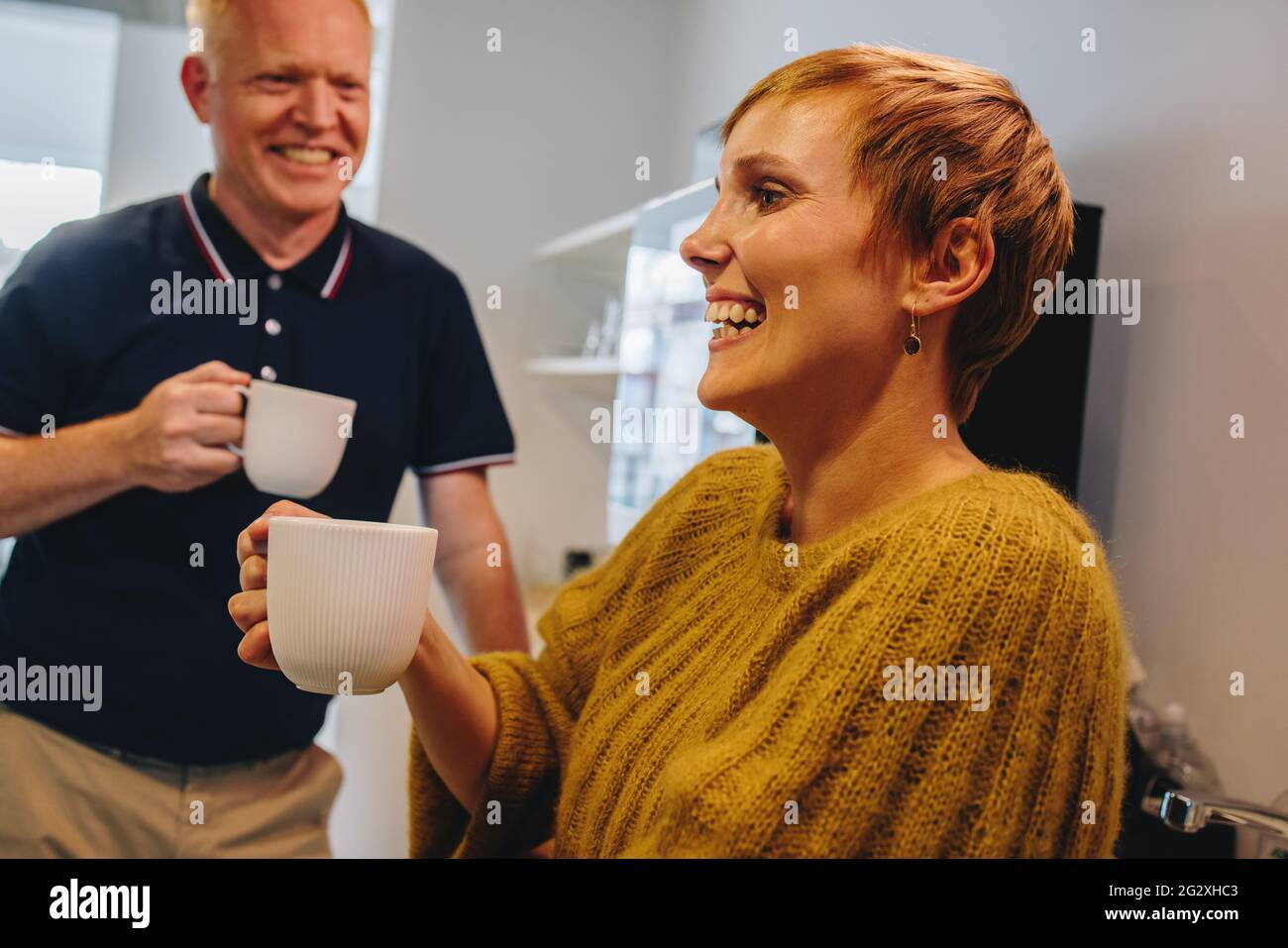 Uomo maturo e giovane donna in piedi e tenendo in mano la tazza di caffè in ufficio. Dirigenti allegri che si levano in piedi e che hanno una pausa caffè in ufficio. Foto Stock