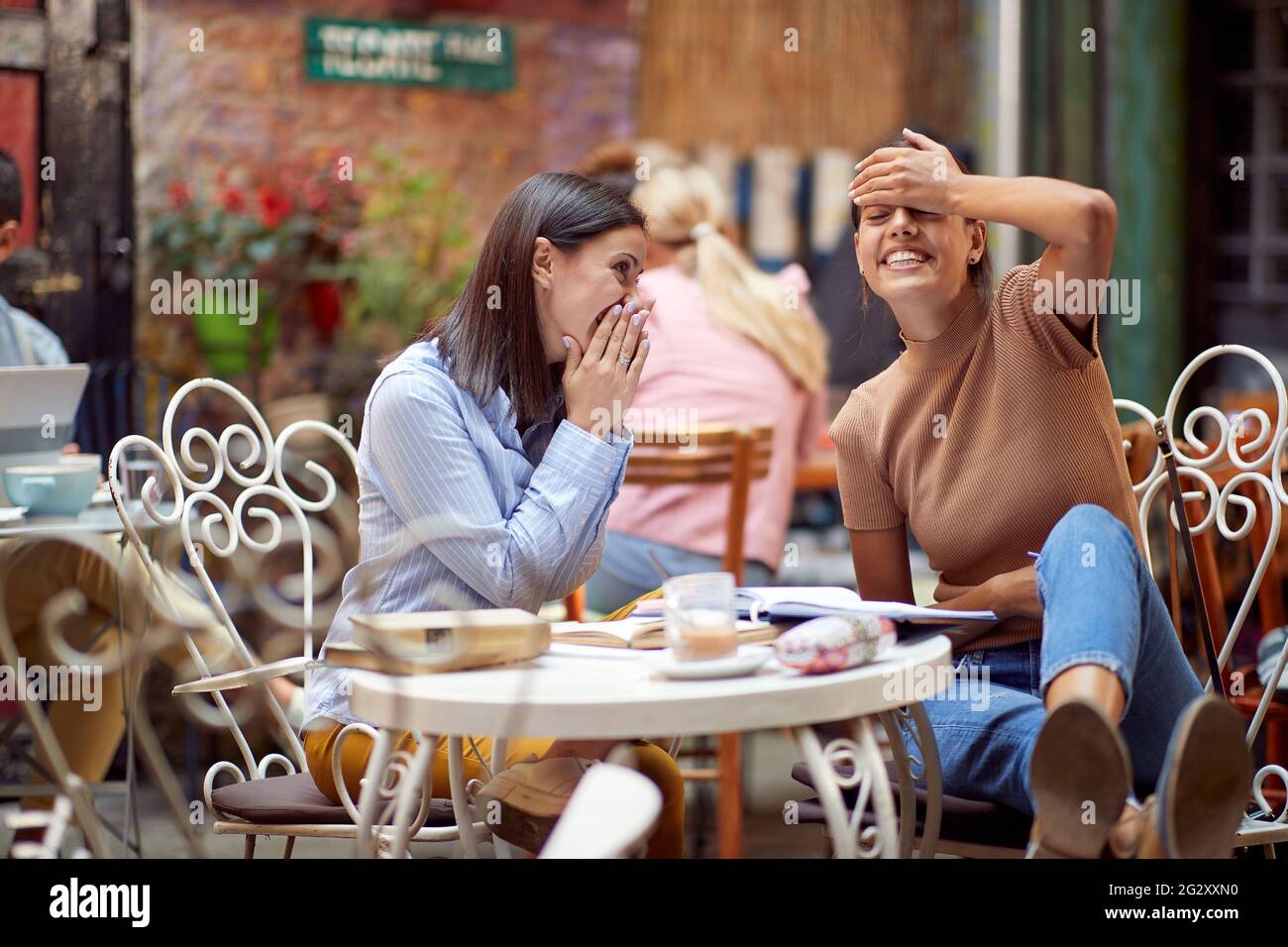 giovane donna caucasica adulta che racconta un pettegolezzo timido alla sua amica femminile al posto pubblico nel caffè all'aperto Foto Stock