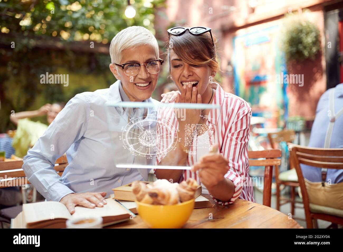 donna caucasica anziana che guarda la scheda astrologica su un blocco note trasparente insieme a una giovane donna adulta. tecnologia di nuova generazione Foto Stock