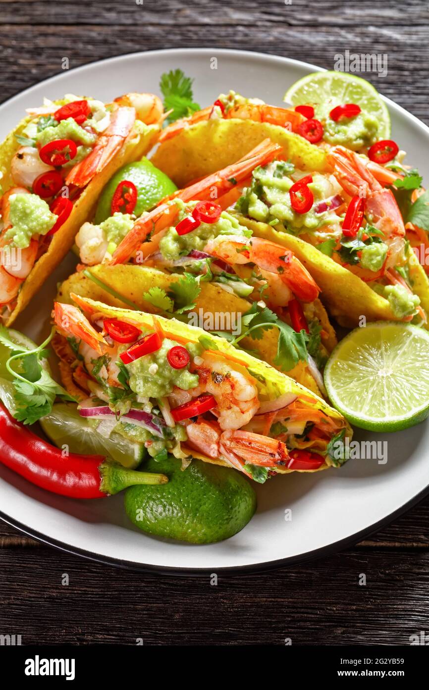 primo piano di conchiglie di taco con gamberi alla griglia, insalata di cavolo, lime e guacamole su un piatto su un tavolo di legno Foto Stock