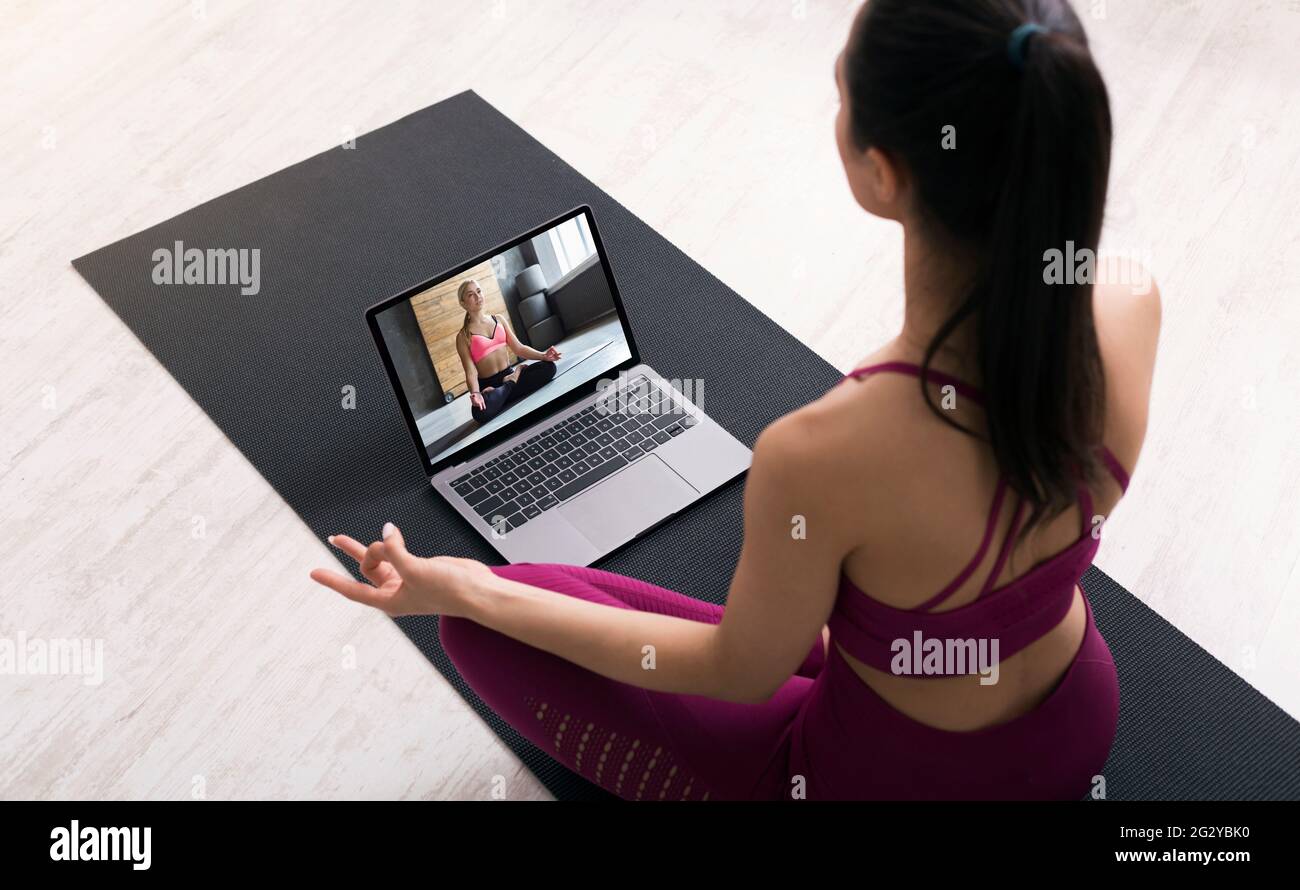 Sopra la vista della giovane donna che fa esercizi respiratori o meditazione, seguendo video tutorial sul laptop a casa Foto Stock