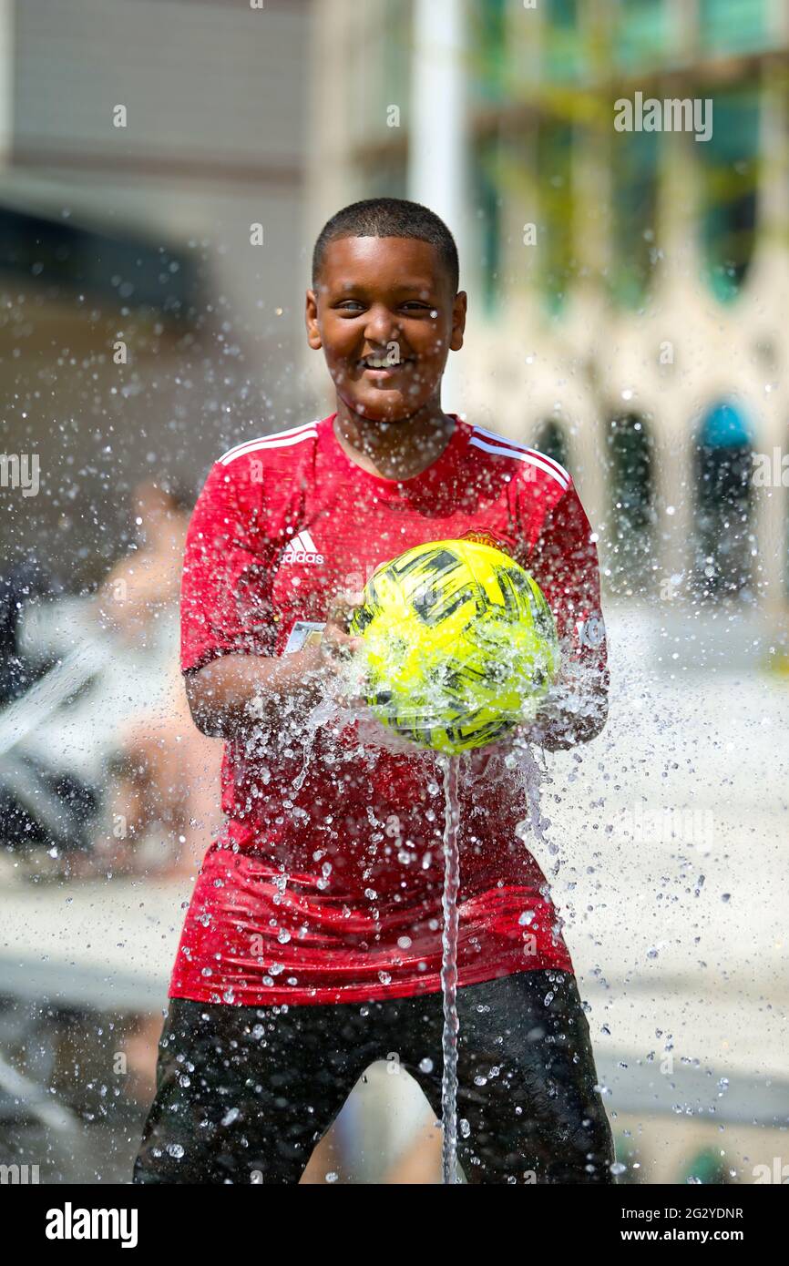 Birmingham, Regno Unito. 13 giugno 2021. Baslel, 11 anni, ha un'ora di calcio nelle fontane della piazza del Centenario di Birmingham, in quello che potrebbe essere il giorno più caldo dell'anno finora. Credit: Peter Lopeman/Alamy Live News Foto Stock