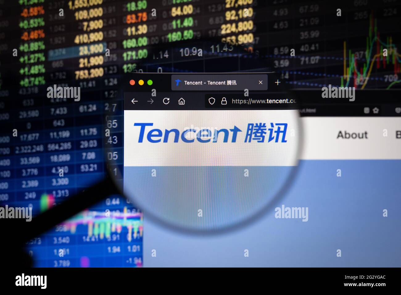Tencent logo aziendale su un sito web con sviluppi sfocati del mercato azionario in background, visto su uno schermo del computer attraverso una lente di ingrandimento Foto Stock