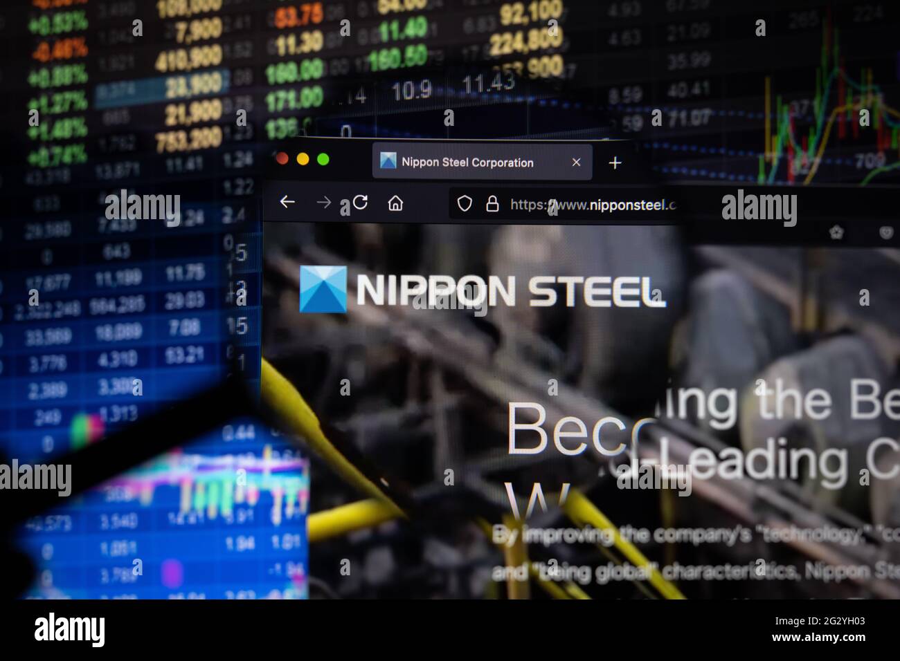 Nippon Steel logo aziendale su un sito web con sviluppi del mercato azionario sfocato in background, visto su uno schermo del computer attraverso una lente di ingrandimento Foto Stock