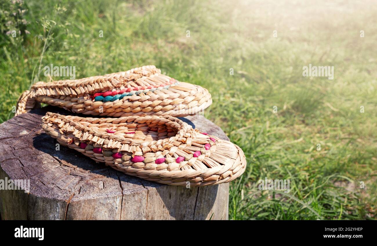 Le scarpe in ghisa intrecciate con materiali naturali giacciono su un  moncone sullo sfondo sfocato della natura, spazio di copia. Ciabatte fatte  a mano per sauna o bagno Foto stock - Alamy