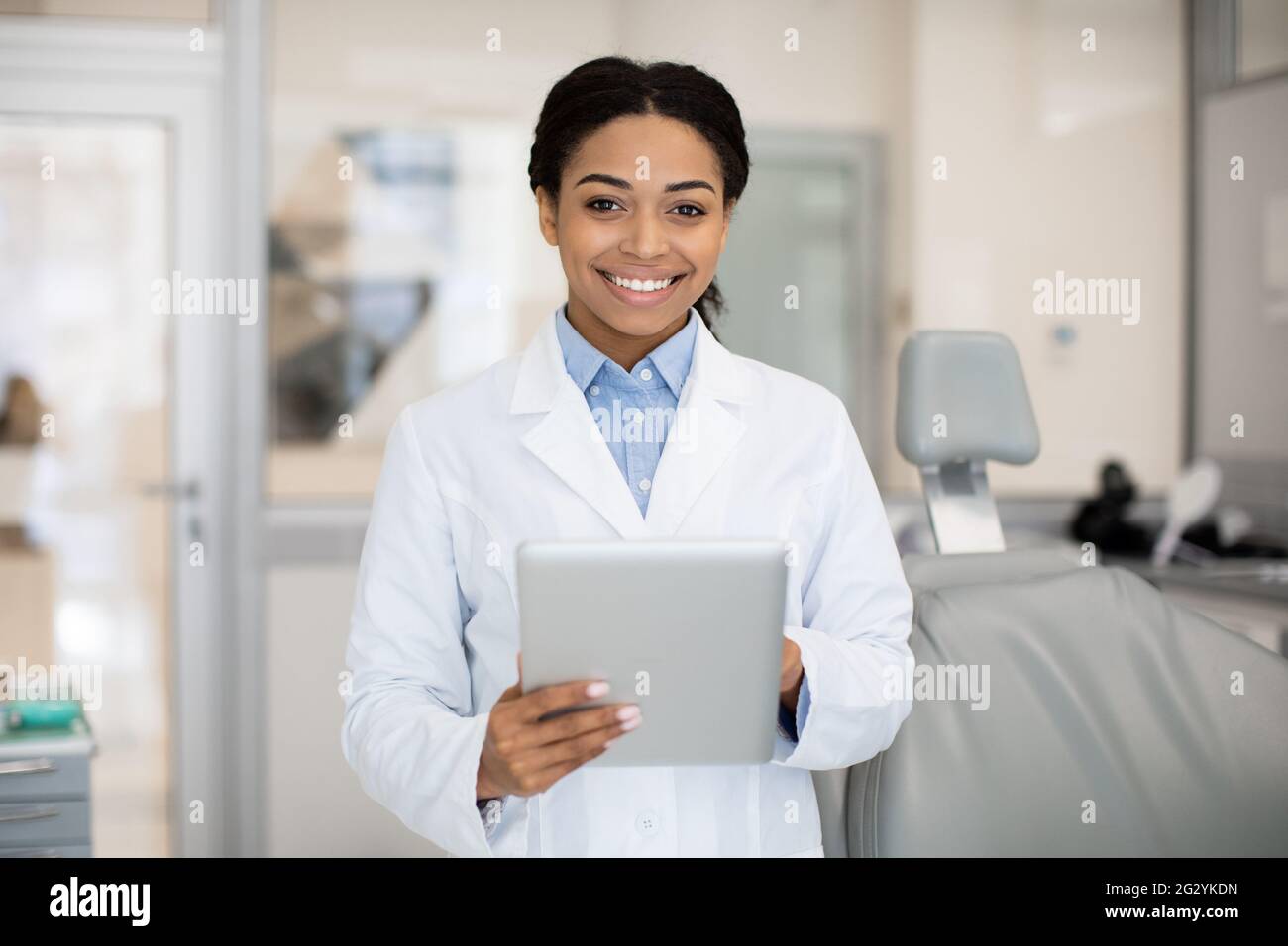 Sorridente dentista femmina nera con tavoletta digitale in posa in clinica stomatologica Foto Stock