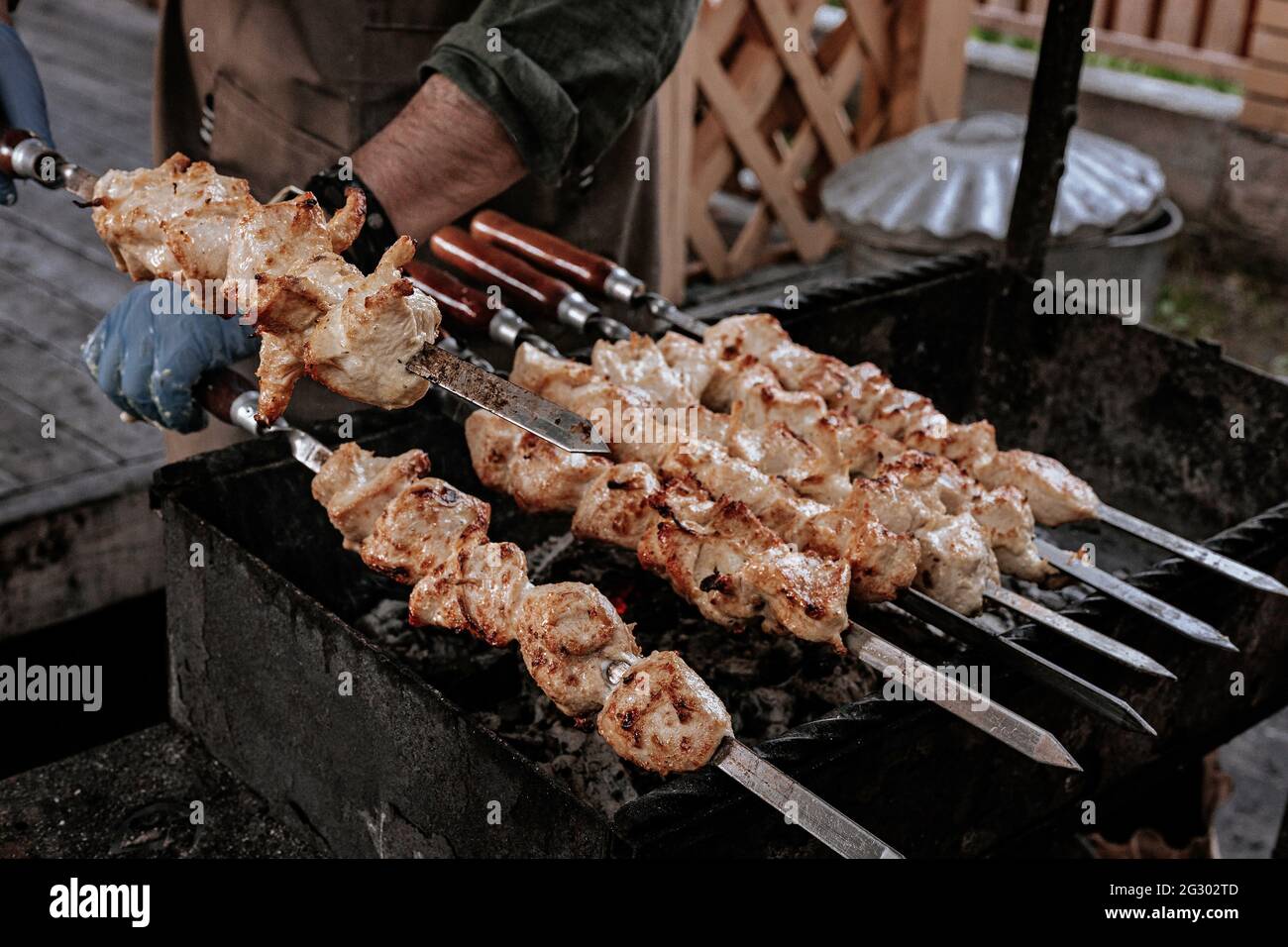 Lo chef prepara il kebab di shish di pollo. Cucina turca di strada. Carne cotta al fuoco, barbecue party nel cortile. Le mani maschili nei guanti tengono il matassa di acciaio Foto Stock