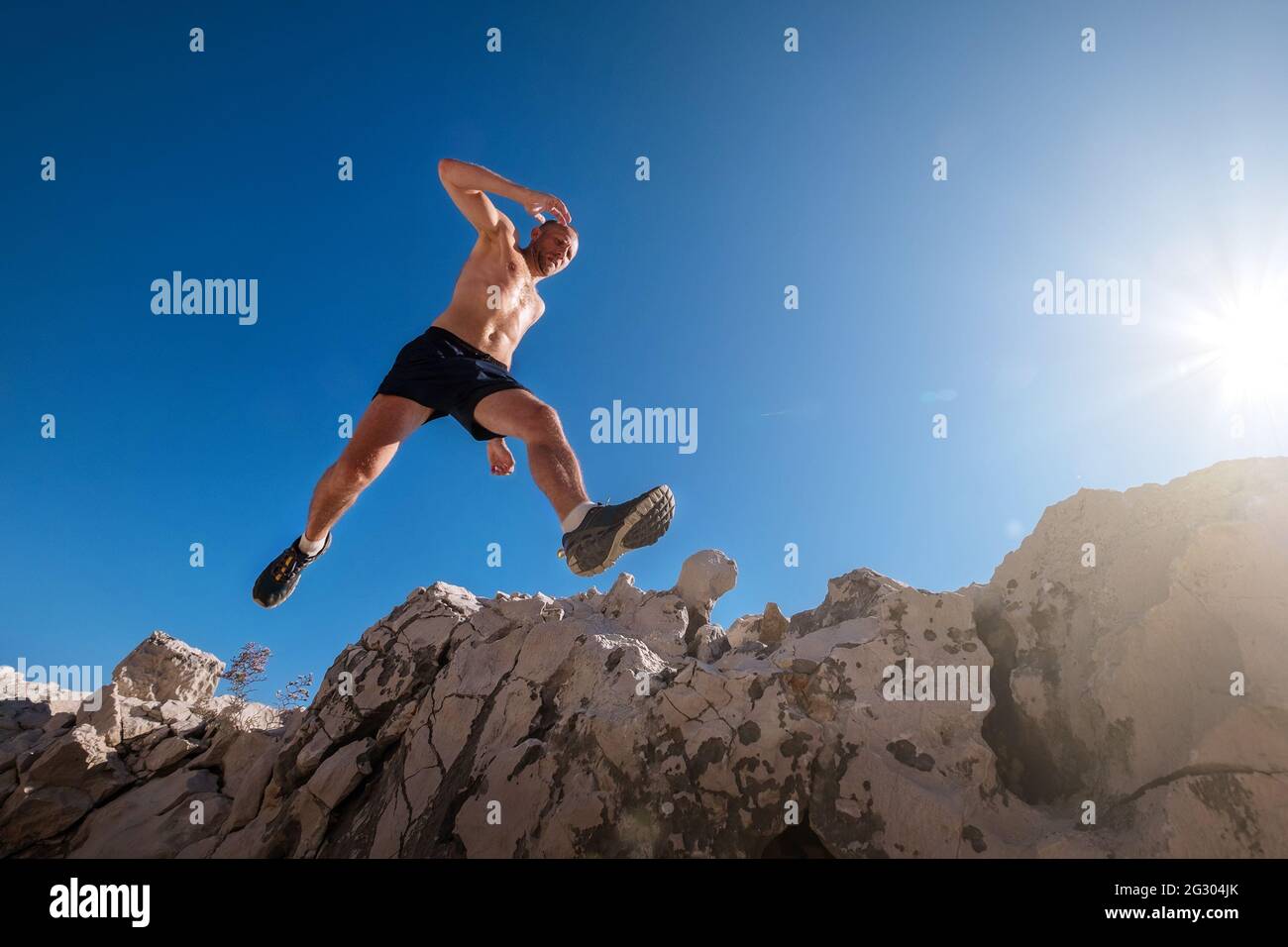 Attivo veloce corsa montagna sudato corpo runner cielo muscolare che salta sopra la scogliera cleft durante il jogging mattutino. Attività sportive per le persone ampio-an Foto Stock