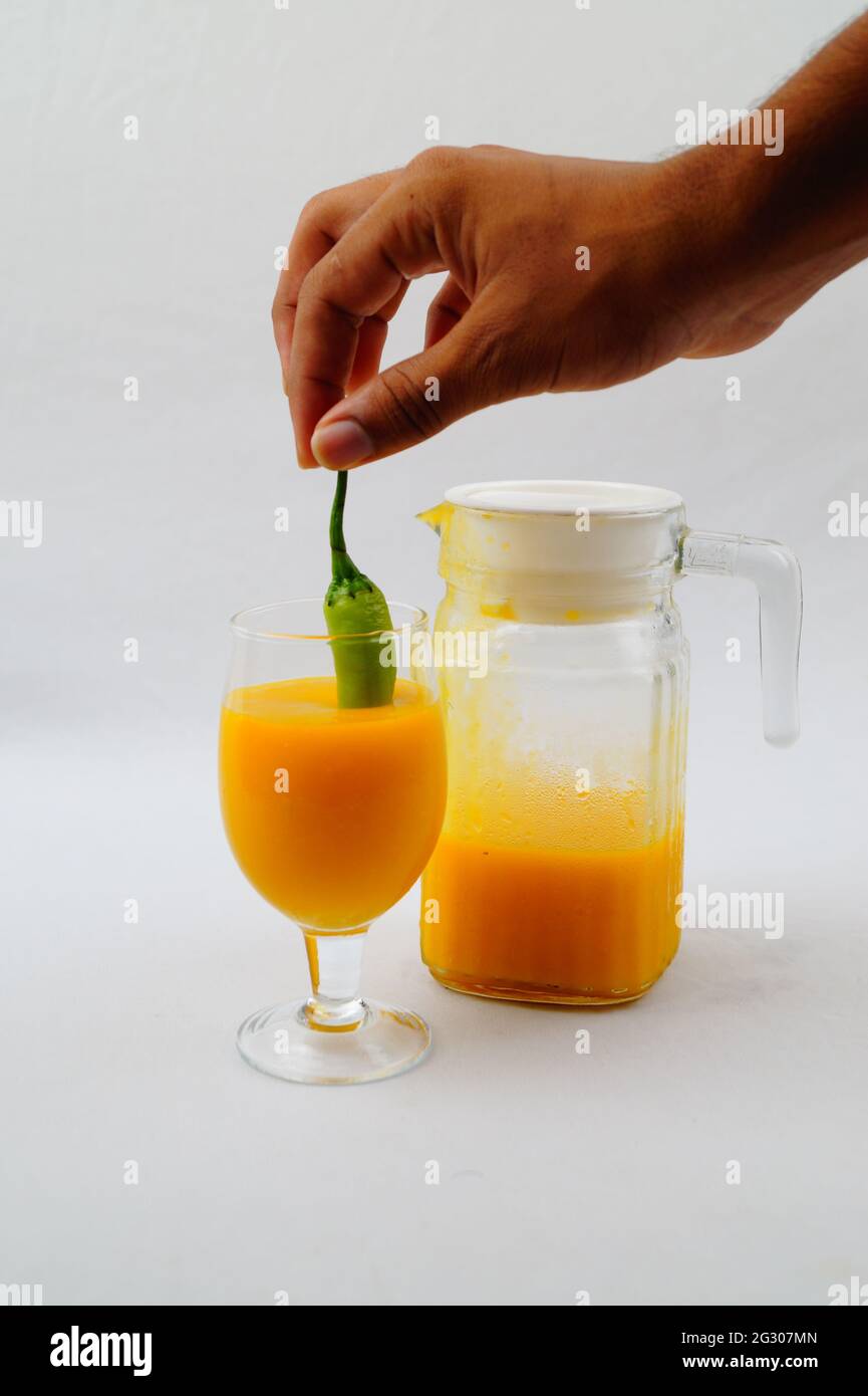 Un primo piano di una persona che immergi un pepe in un succo di mango fresco Foto Stock