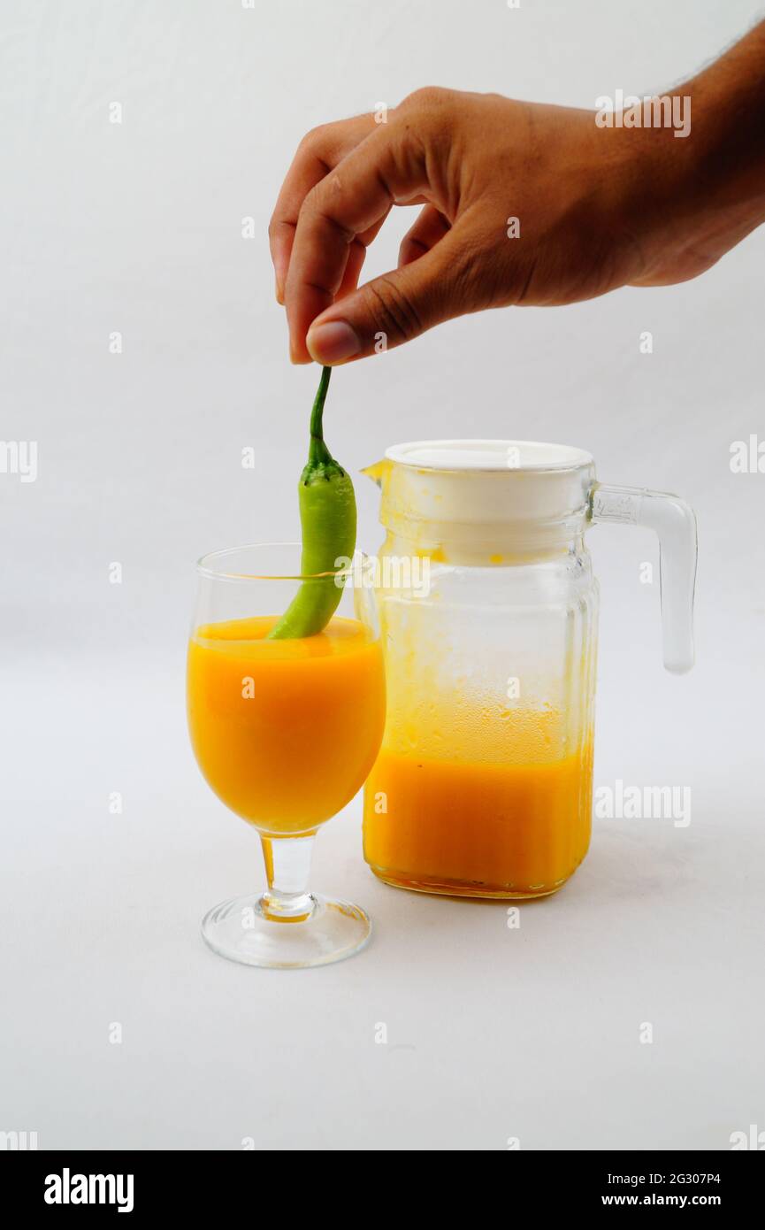 Un primo piano di una persona che immergi un pepe in un succo di mango fresco Foto Stock
