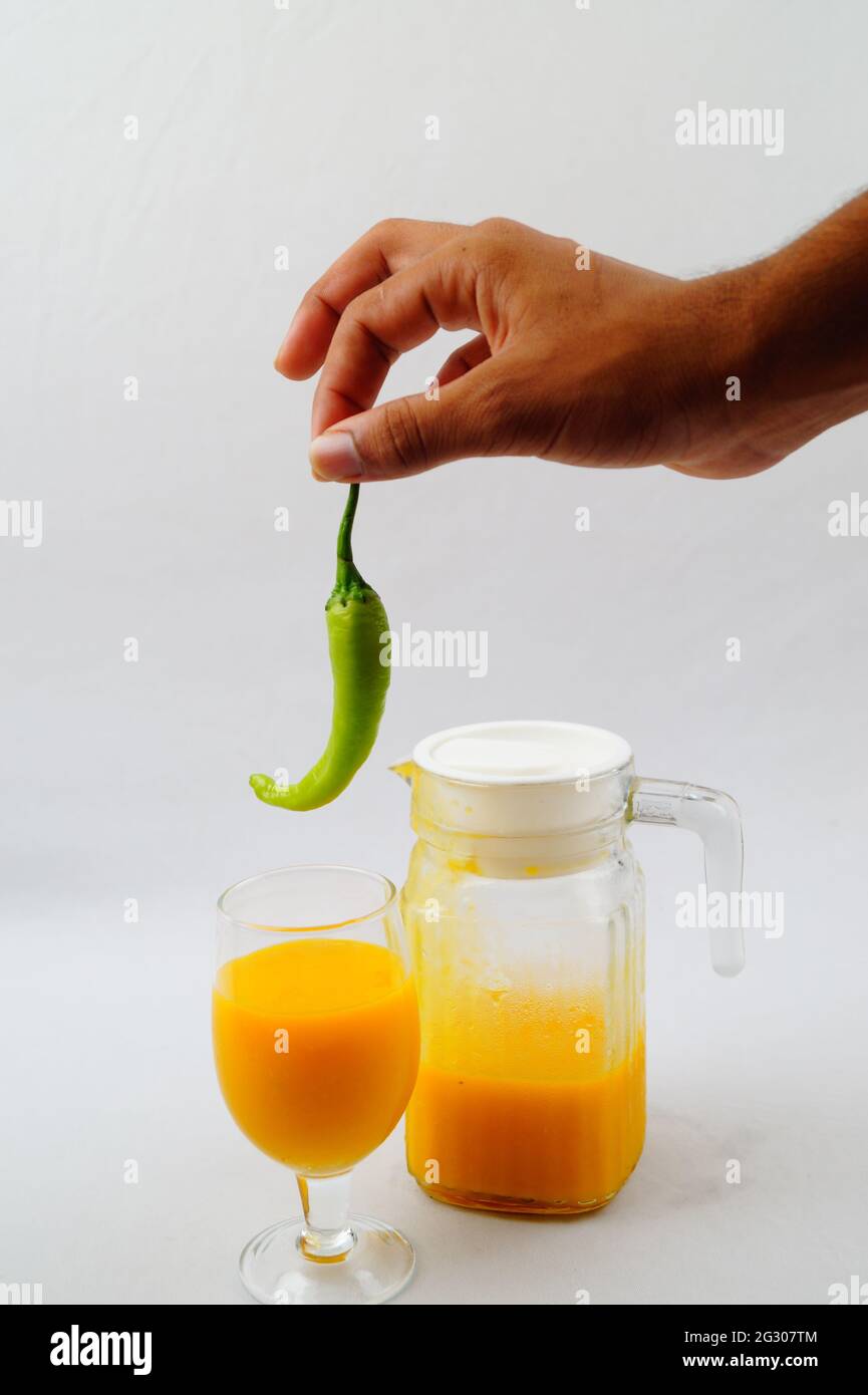 Un primo piano di una persona che tiene un pepe sopra un bicchiere di succo di mango fresco Foto Stock