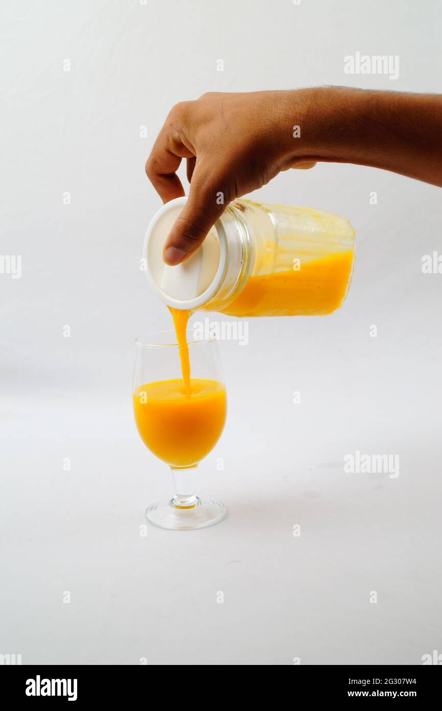 Un primo piano di una persona che versa il succo di mango fresco in un bicchiere Foto Stock