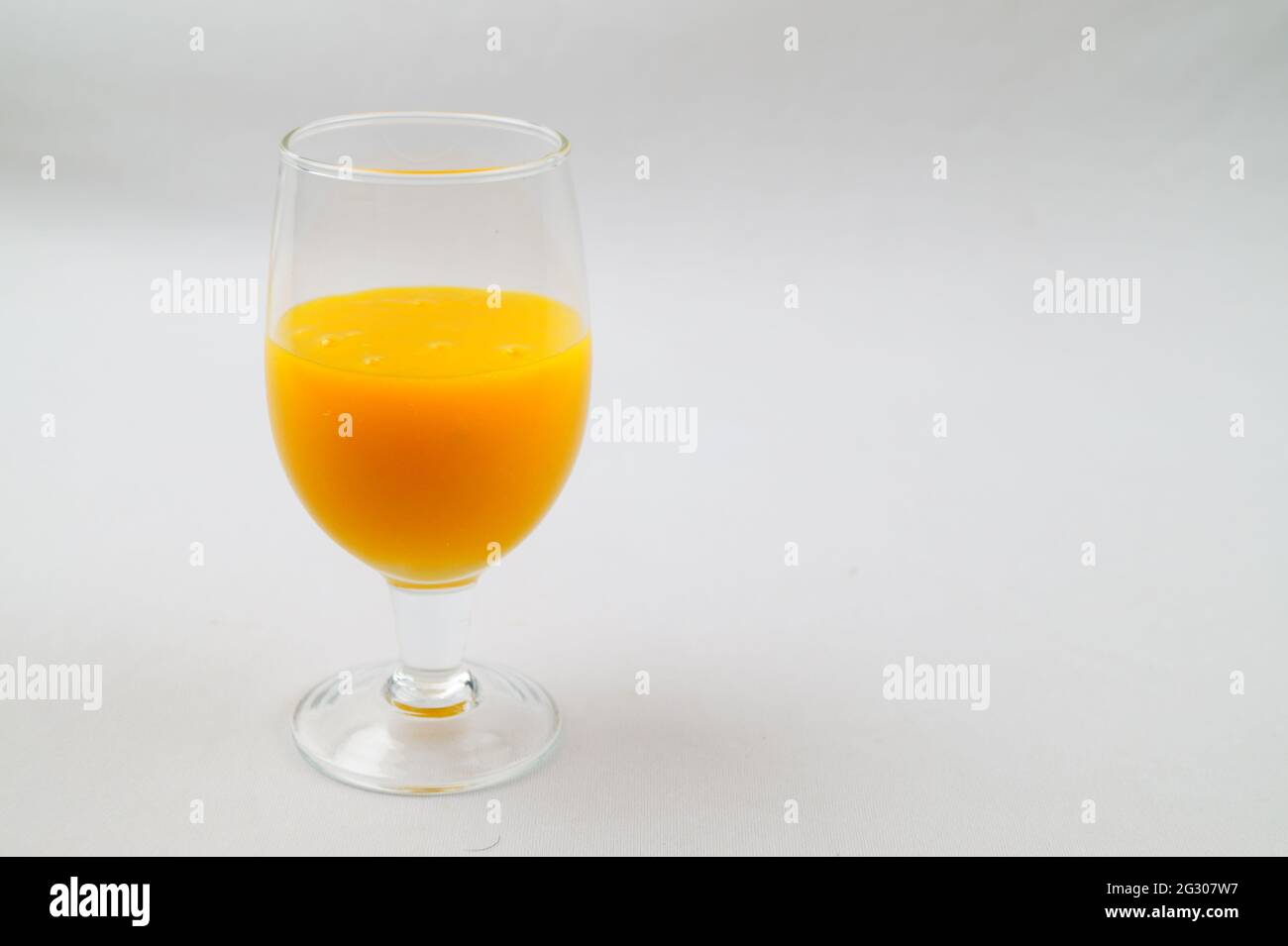 Una selezione di un bicchiere di succo di mango fresco su una superficie bianca Foto Stock